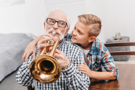 Grandfather playing trumpet while smiling boy is hugging him from behindの写真素材