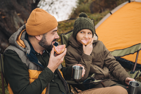Father and son drinking tea and eating sandwiches with sausage on a natureの写真素材