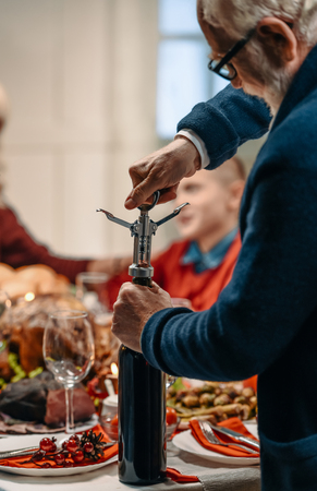senior man opening bottle of wine on christmas dinnerの写真素材
