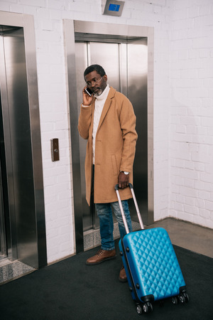 Middle aged man waiting for lift standing with wheeled bagの写真素材