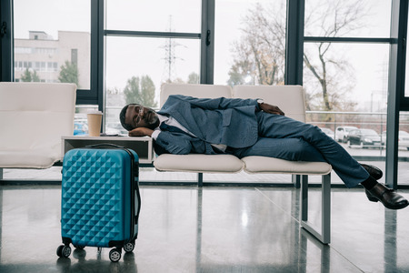 Middle aged African american businessman napping on chairs at airportの写真素材