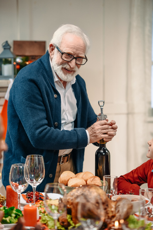 happy senior man opening wine bottle on holiday dinnerの写真素材