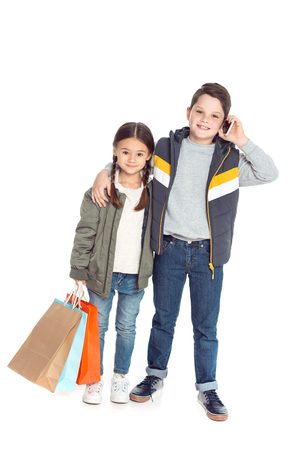 sister holding shopping bags while brother talking on smartphone, isolated on whiteの写真素材