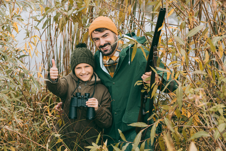 Son showing thumb up while standing with father at huntの写真素材