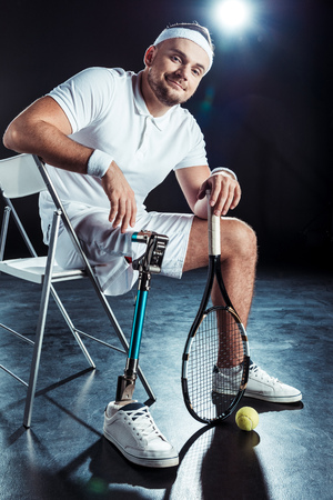  tennis player with tennis racket looking at camera while resting on chairの写真素材