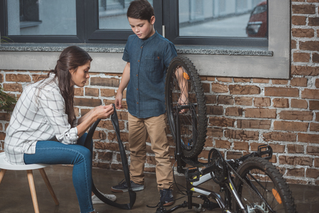 Young woman helping her little son to fix his bicycle wheelの写真素材