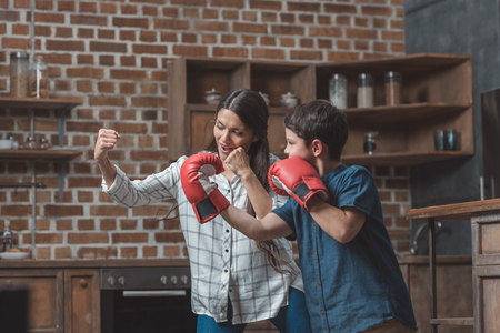 Little boy wearing boxing gloves and his mother practicing punches in kitchenの写真素材