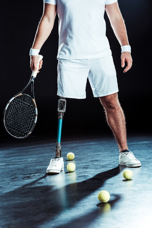 cropped shot of   tennis player holding tennis racket with tennis balls on floorの写真素材