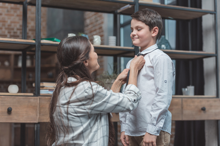 Mother helping her little son get dressed and tie a necktieの写真素材