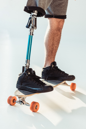 cropped shot of man with leg prosthesis standing on skateboard isolated on whiteの写真素材