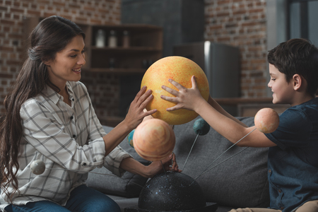 Little boy and his mother building a solar system model together in living roomの写真素材