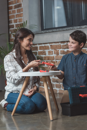 Young woman handing pliers to her little son while sitting on floor in living roomの写真素材