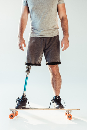 cropped shot of man with leg prosthesis standing on skateboard isolated on whiteの写真素材