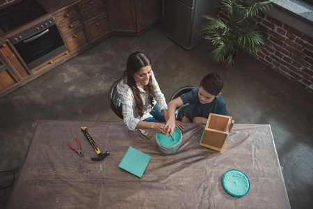 Little son and his beautiful mother sitting at kitchen table and painting a wooden birdhouseの写真素材