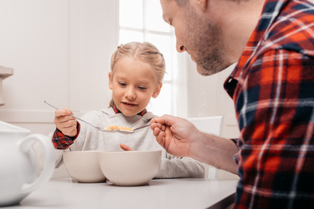 cropped shot of father and little daughter eating corn flakes at breakfastの写真素材