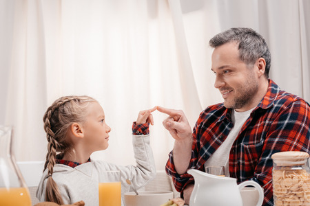 happy father and daughter touching fingers while having breakfast togetherの写真素材