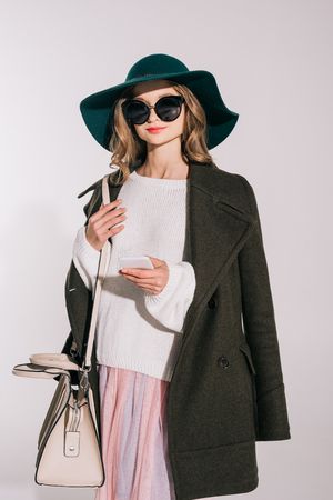 beautiful teenage girl in black hat and sunglasses using smartphone isolated on grey の写真素材