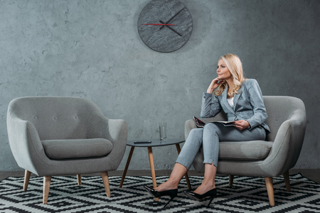 businesswoman sitting in armchair with magazine at office lobby