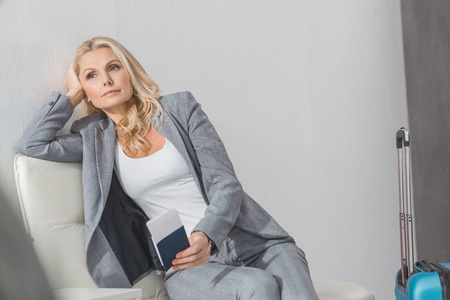 thoughtful mature businesswoman with flight ticket and luggage waiting for tripの写真素材