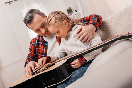 father teaching adorable little daughter playing acoustic guitar at homeの写真素材