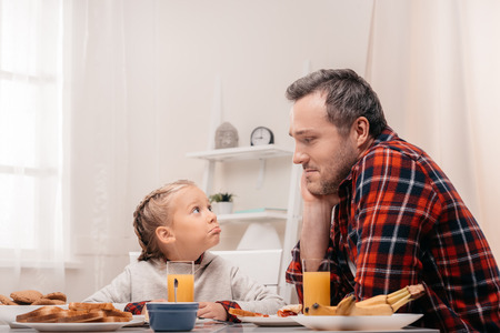 father and daughter looking at each other while having breakfast togetherの写真素材