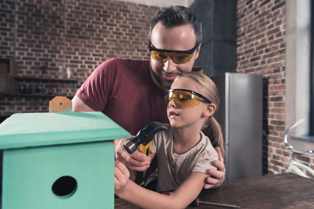 Father helping daughter use drill to make birdhouse in the kitchen の写真素材