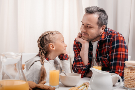 happy father and daughter looking at each other while having breakfast togetherの写真素材