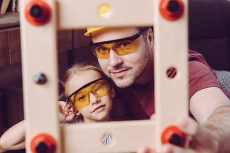 Father and daughter posing in yellow glasses with self-made wooden frame の写真素材
