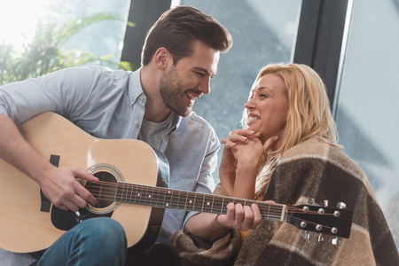 smiling handsome man playing guitar for girlfriend at homeの写真素材