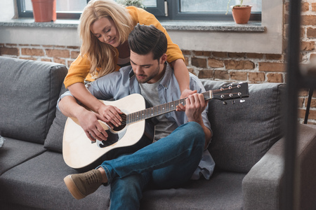 young beautiful couple playing guitar together at home on couchの写真素材