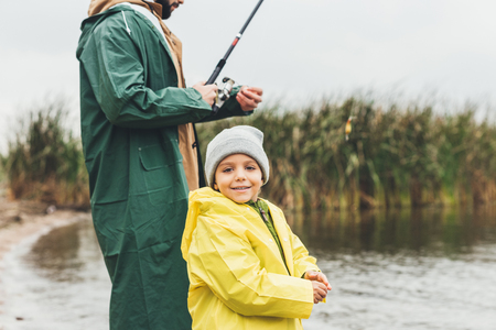 happy son fishing with father in raincoats on autumn dayの写真素材