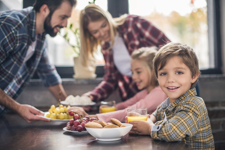 selective focus of little boy looking at camera while having breakfast together with family at homeの写真素材