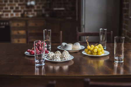 selective focus of fresh grapes, desserts and empty glasses on wooden table in kitchen の写真素材