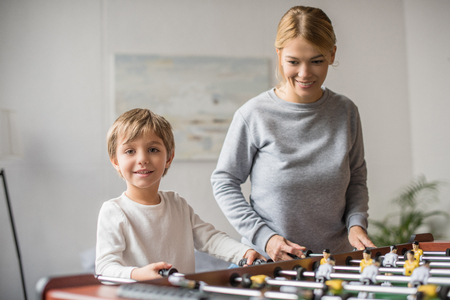 portrait of smiling mother and little son playing table football together at homeの写真素材