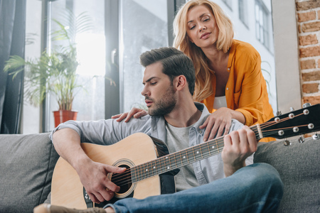 sensual young man playing guitar for girlfriend at homeの写真素材