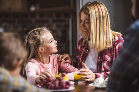 cheerful mother and daughter having breakfast together at homeの写真素材