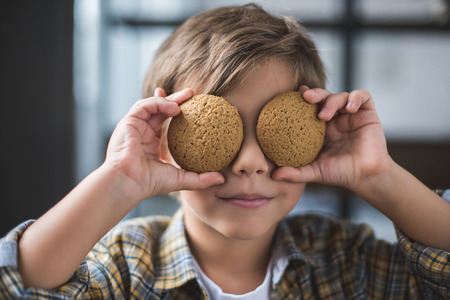 obscured view of little boy covering eyes with cookies in handsの写真素材