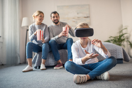 selective focus of parents with popcorn looking at kid playing in vr headset at homeの写真素材