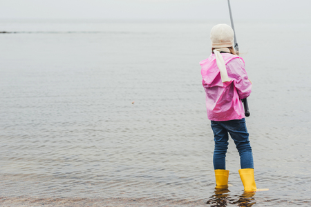 back view of lonely little girl fishing in seaの写真素材