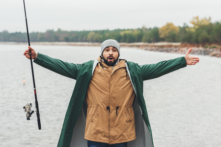 bearded man with fishing rod showing size of fish with handsの写真素材