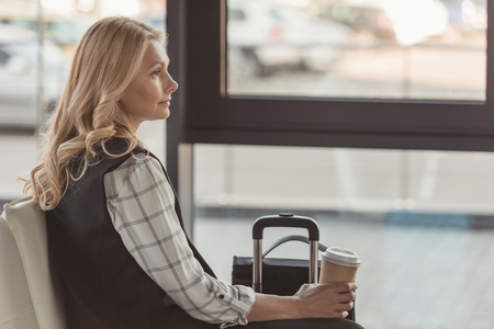 attractive woman with suitcase and coffee waiting for flightの写真素材
