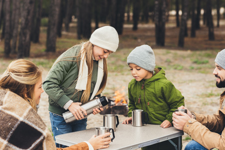happy little girl poring hot drink from thermos for familyの写真素材