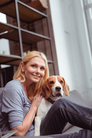 beautiful smiling woman stroking beagle dog at home の写真素材