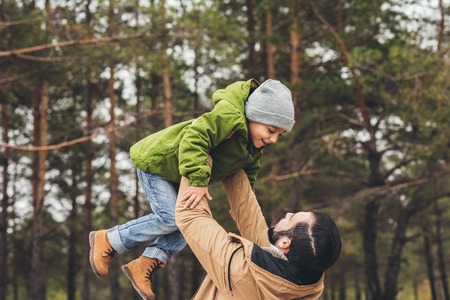 father throwing up his happy little son in pine forestの写真素材