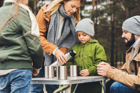 beautiful young mother pouring tea from thermos for kids on camping tripの写真素材