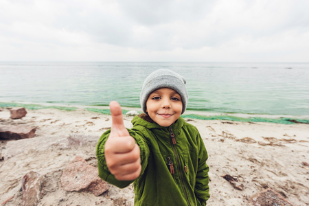 smiling little boy showing thumb up in front of seaの写真素材