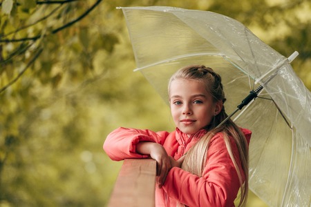 cute little child holding umbrella and looking at camera in autumn parkの写真素材