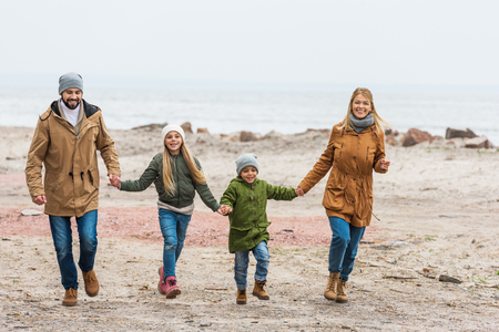 happy beautiful family holding hands and walking by seashore on autumn dayの写真素材