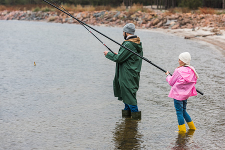 father and daughter fishing together on cold autumn dayの写真素材