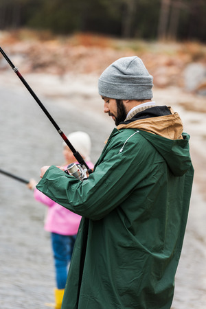 father and daughter fishing together on cold autumn dayの写真素材